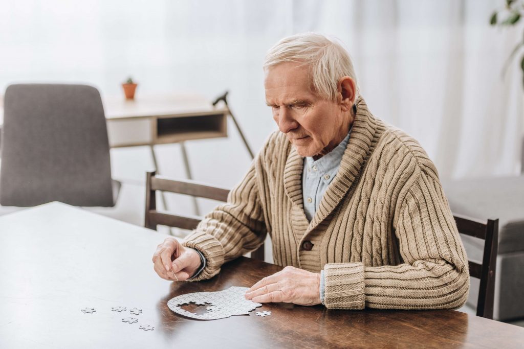 un retraité en pull beige faisant un puzzle